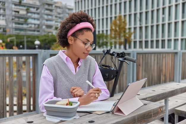 jeune-etudiante-regarde-webinaire-didacticiel-video-concentre-ecran-tablette-ecrit-notes-dans-bloc-notes-informations-projet-posent-exterieur-contre-plan-creation-atmosphere-chaleureuse_273609-54606